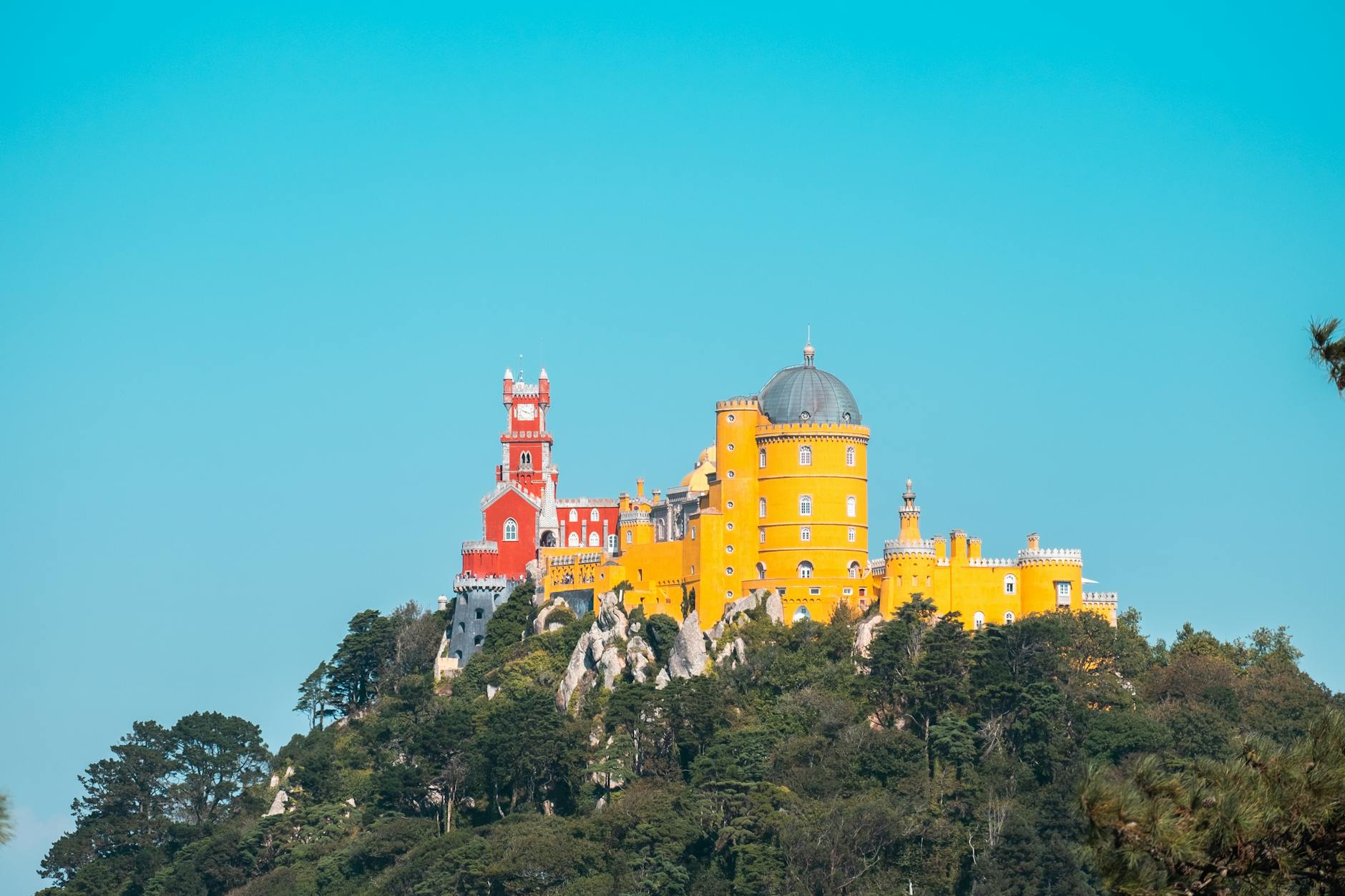 Colorful Pena Palace in Sintra perched on hilltop with mountain forest in background