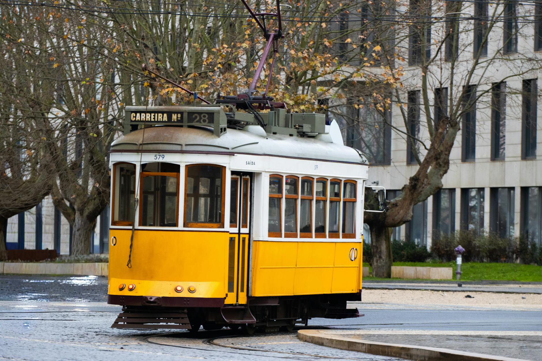 Yellow Lisbon tram 28 climbing a sunlit cobbled street in late spring