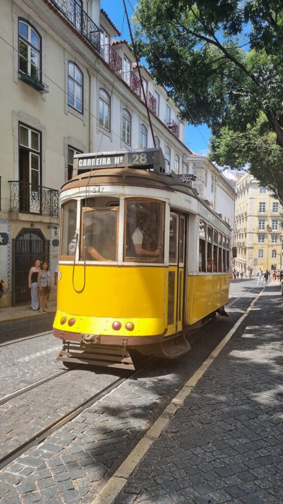 Iconic yellow Tram 28 navigating the charming narrow streets of Lisbon on a sunny day