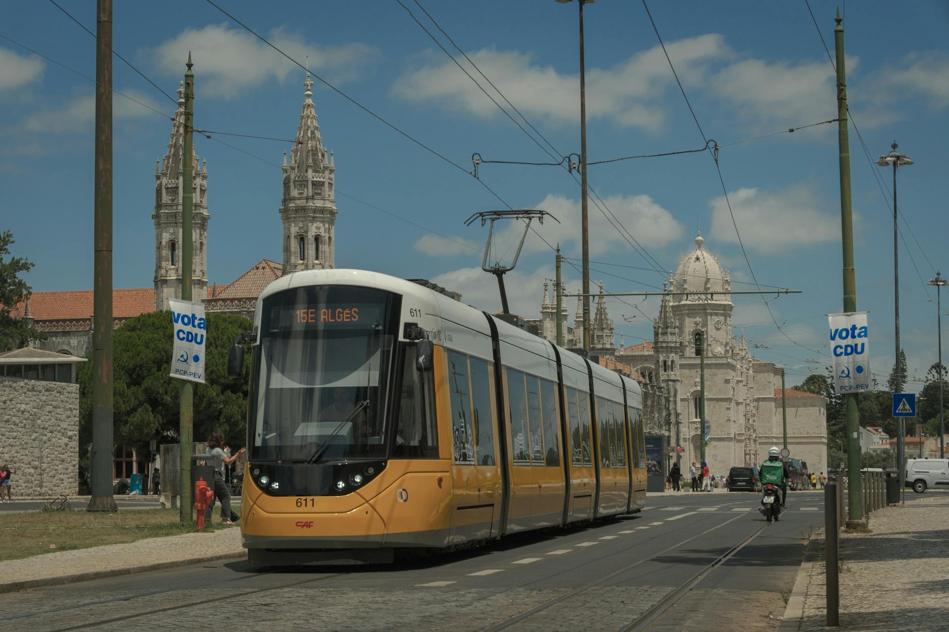Yellow tram passing Jerónimos Monastery in Belém Lisbon under blue sky
