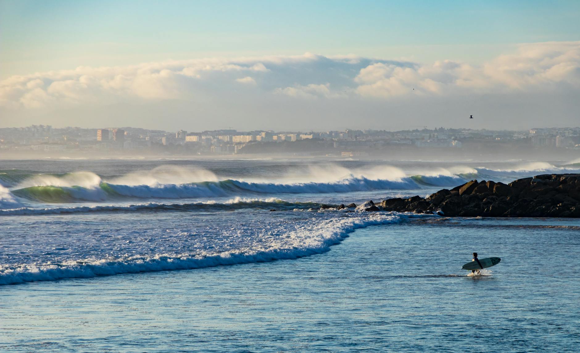 Surfer carrying board toward Atlantic waves at Costa da Caparica beach Portugal