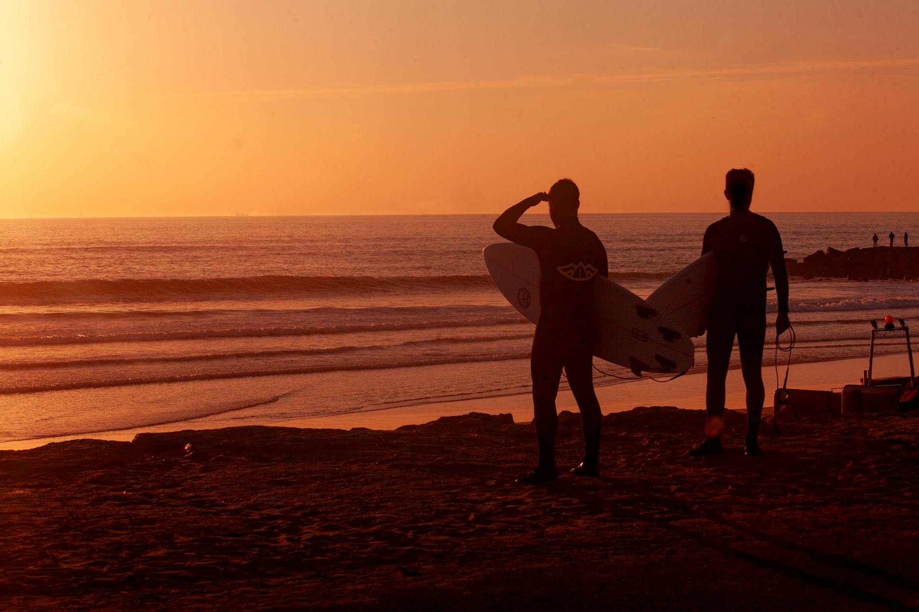 Silhouetted surfers with boards watching sunset at Costa da Caparica Portugal