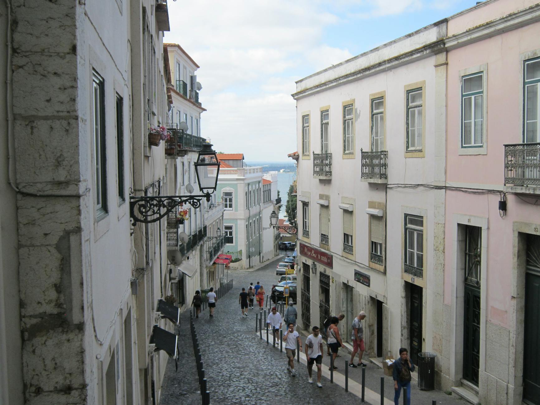 Narrow Lisbon alley with old tiled buildings and sea view at the end