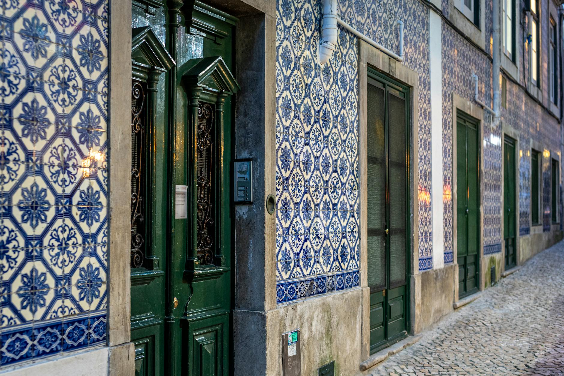 Blue and white azulejo tiled building on a Lisbon street with green doorways