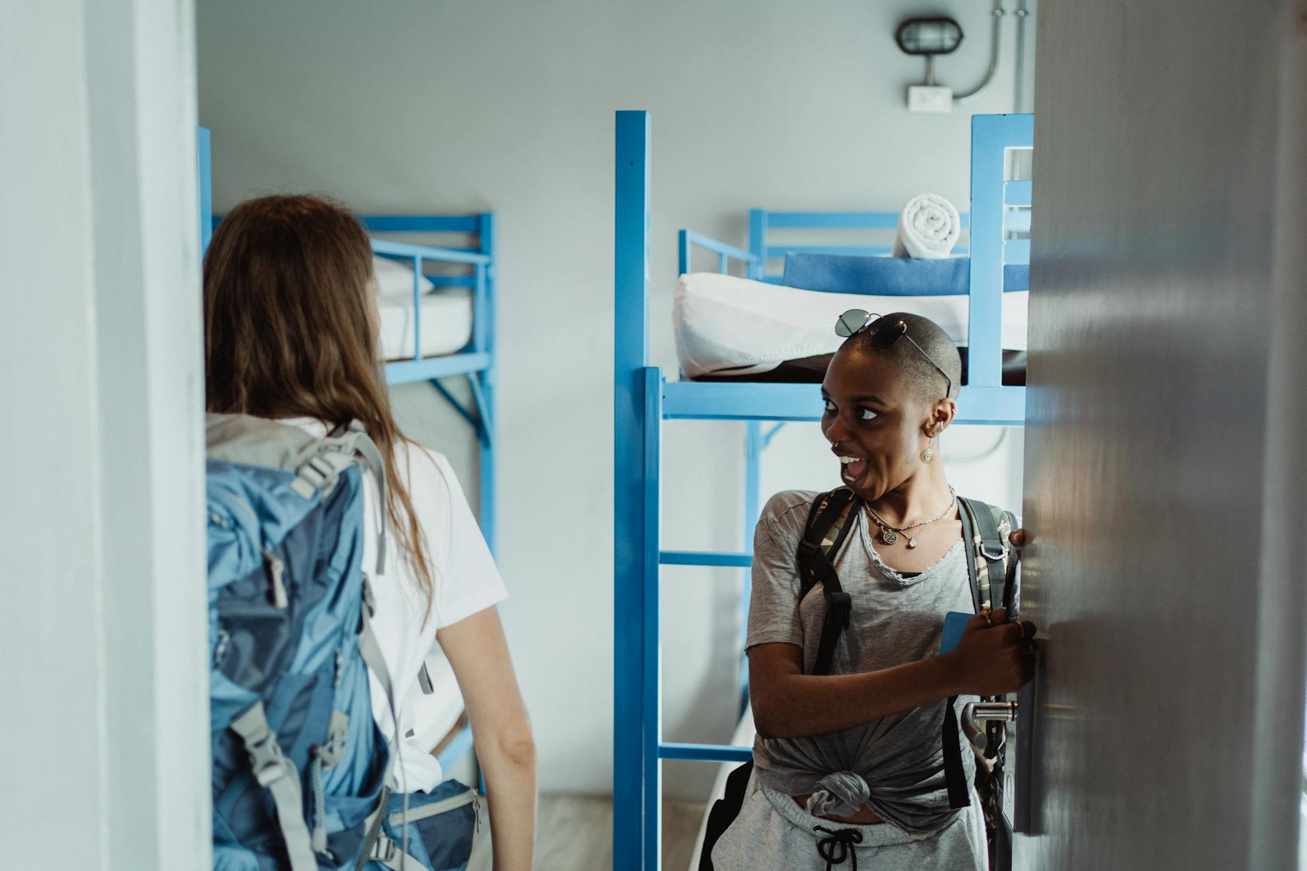 Two backpackers arriving at a bright hostel dorm room in Lisbon