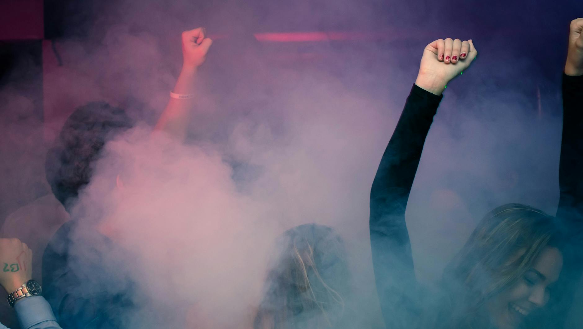 Crowd of people dancing at a Lisbon nightclub with hands raised under coloured lights
