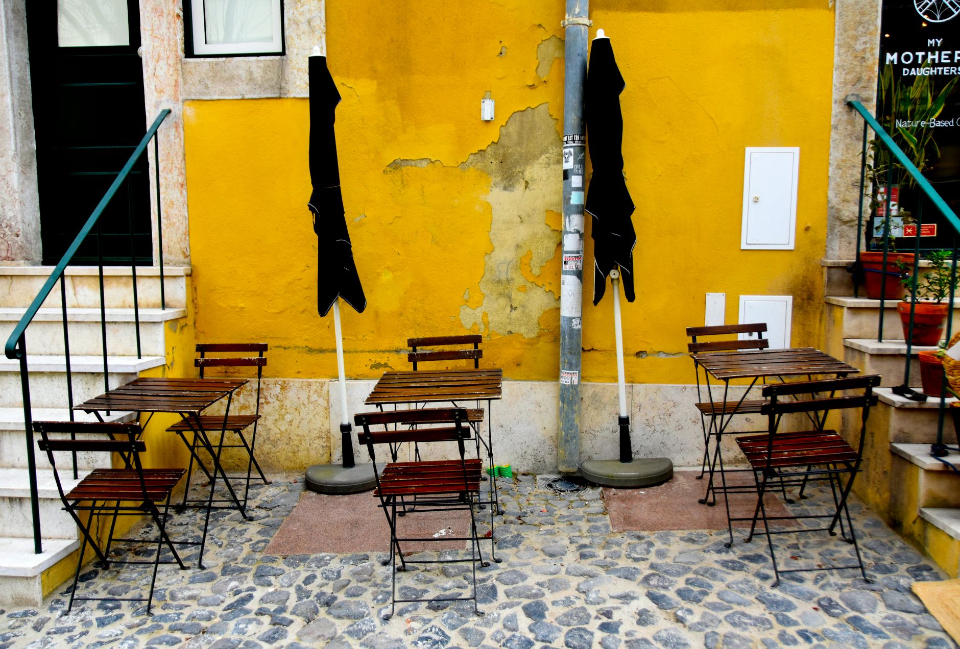 Outdoor cafe on cobblestone street in Lisbon with yellow walls and chairs