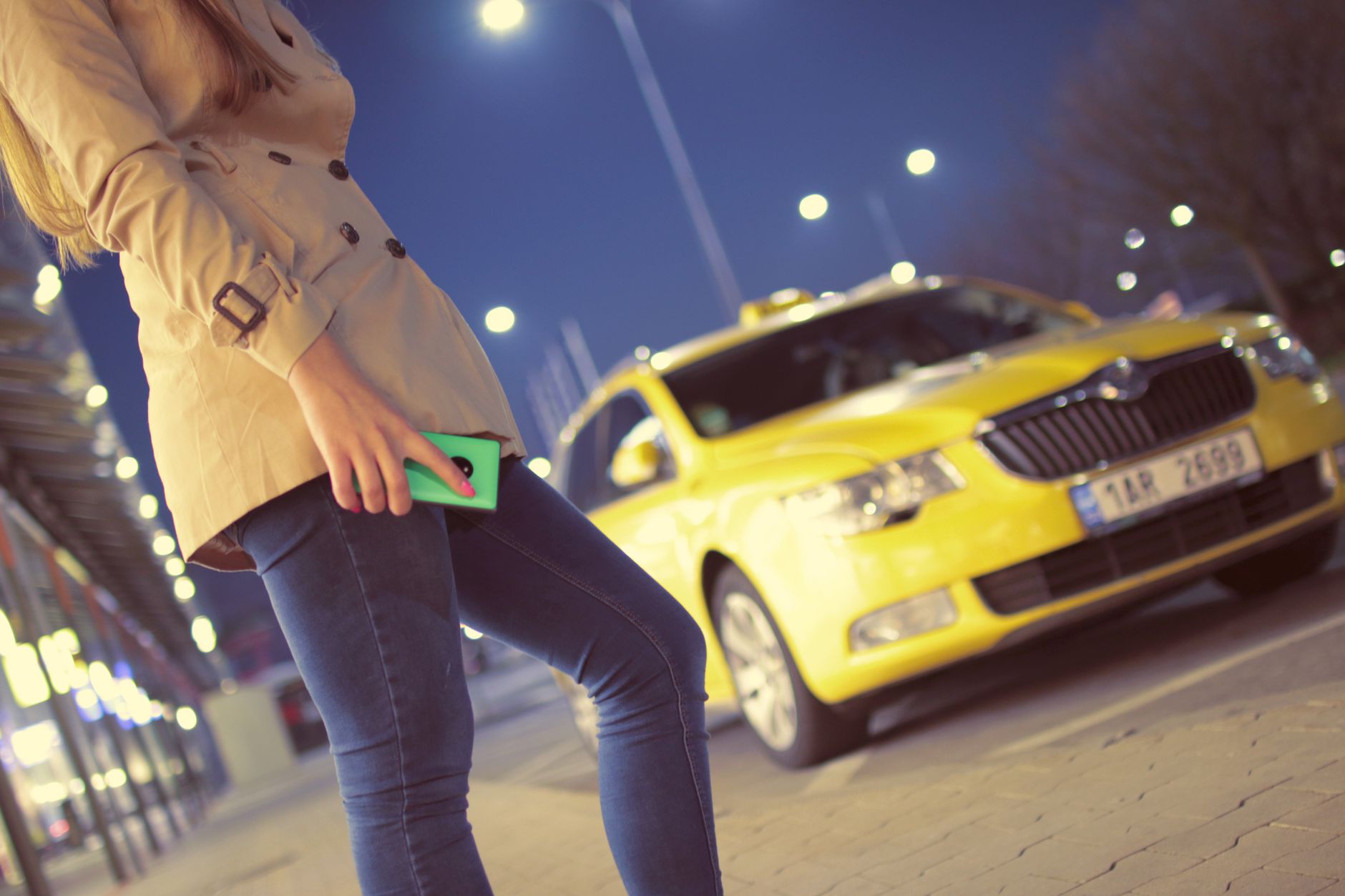 Woman with smartphone hailing a taxi at night — using Uber or Bolt in Lisbon
