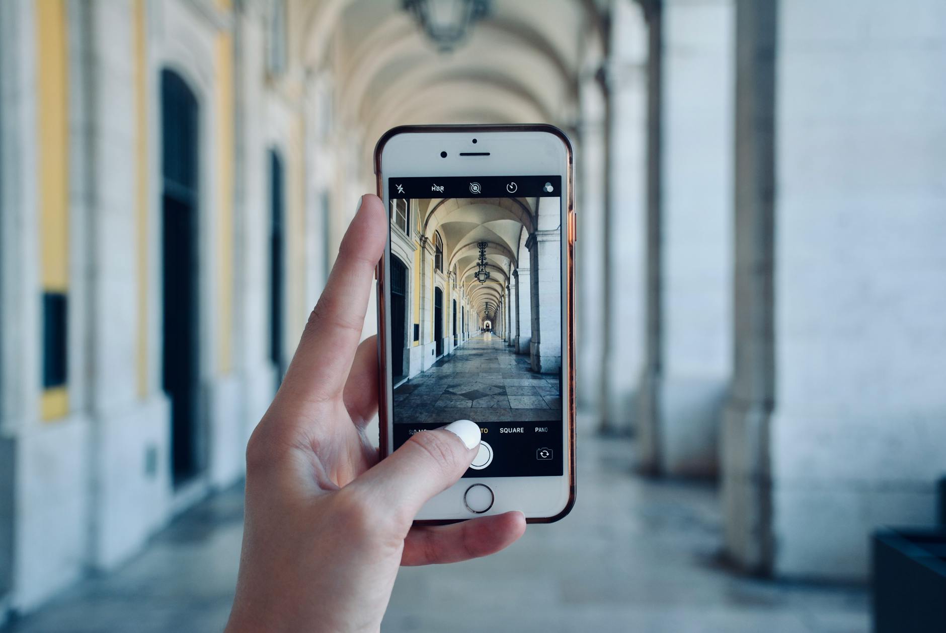 Hand holding smartphone photographing Lisbon Praca do Comercio colonnade arches