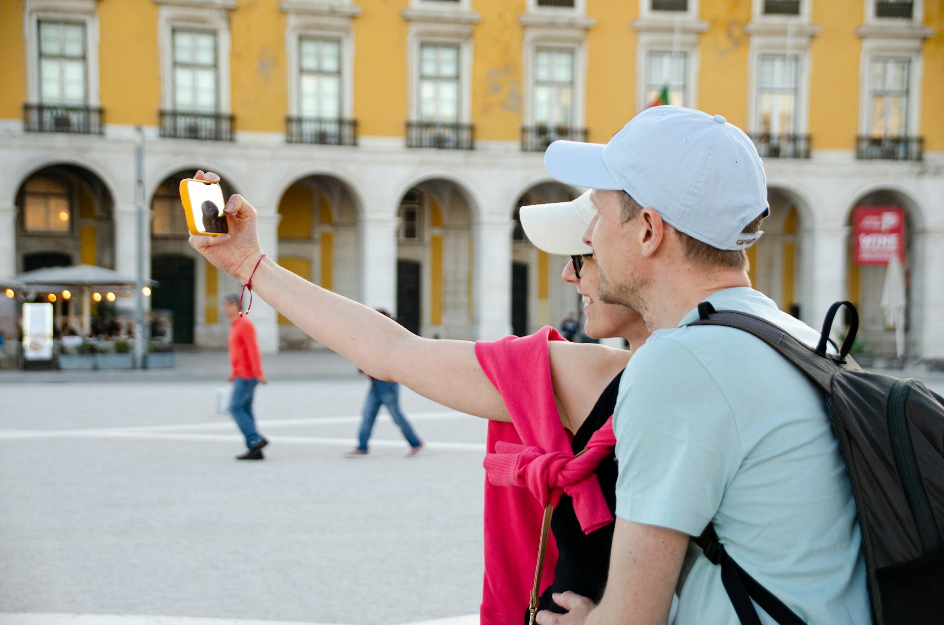 Couple taking selfie at Praca do Comercio in Lisbon with historic architecture behind them