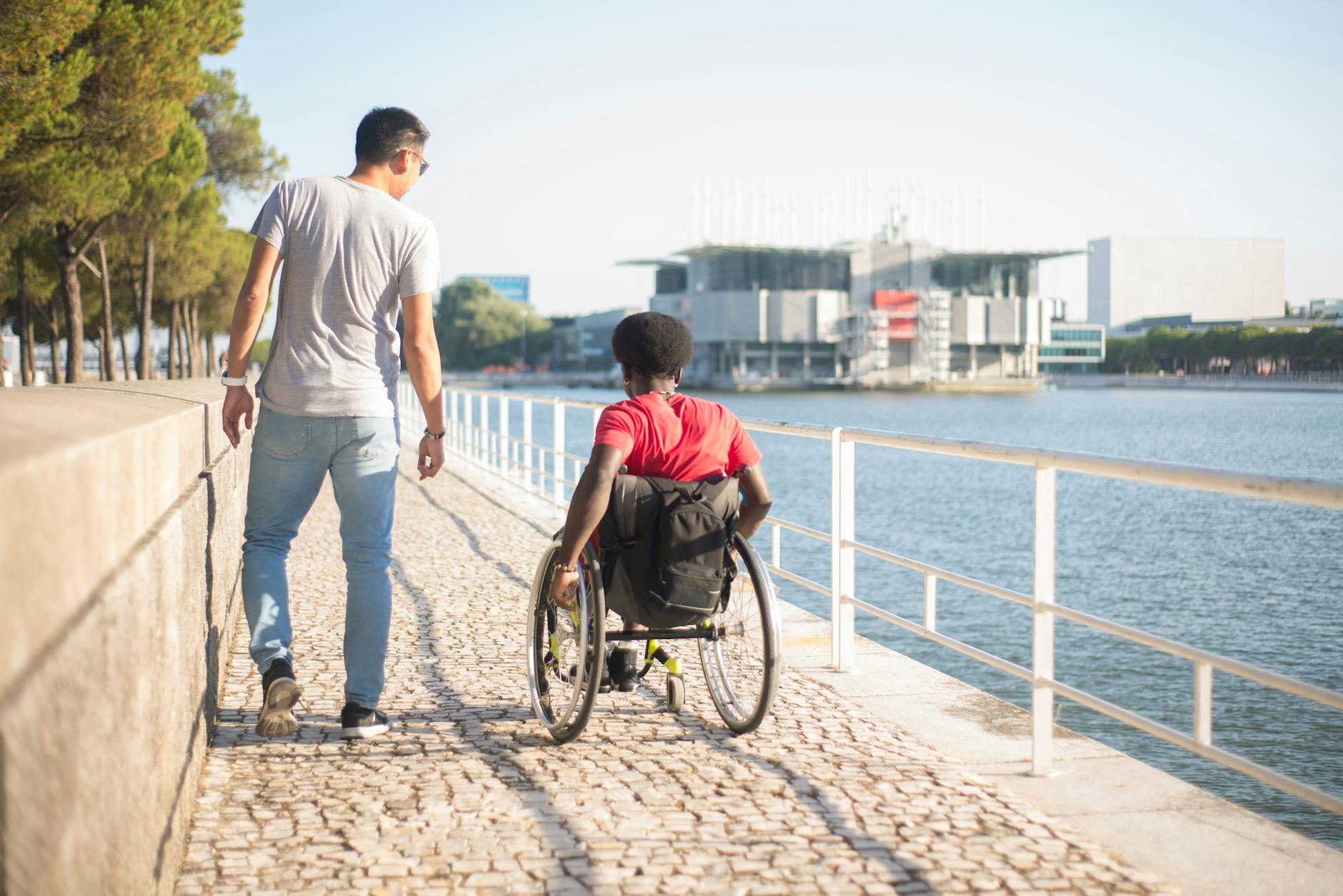 Wheelchair user and friend walking along Lisbon's accessible riverside promenade