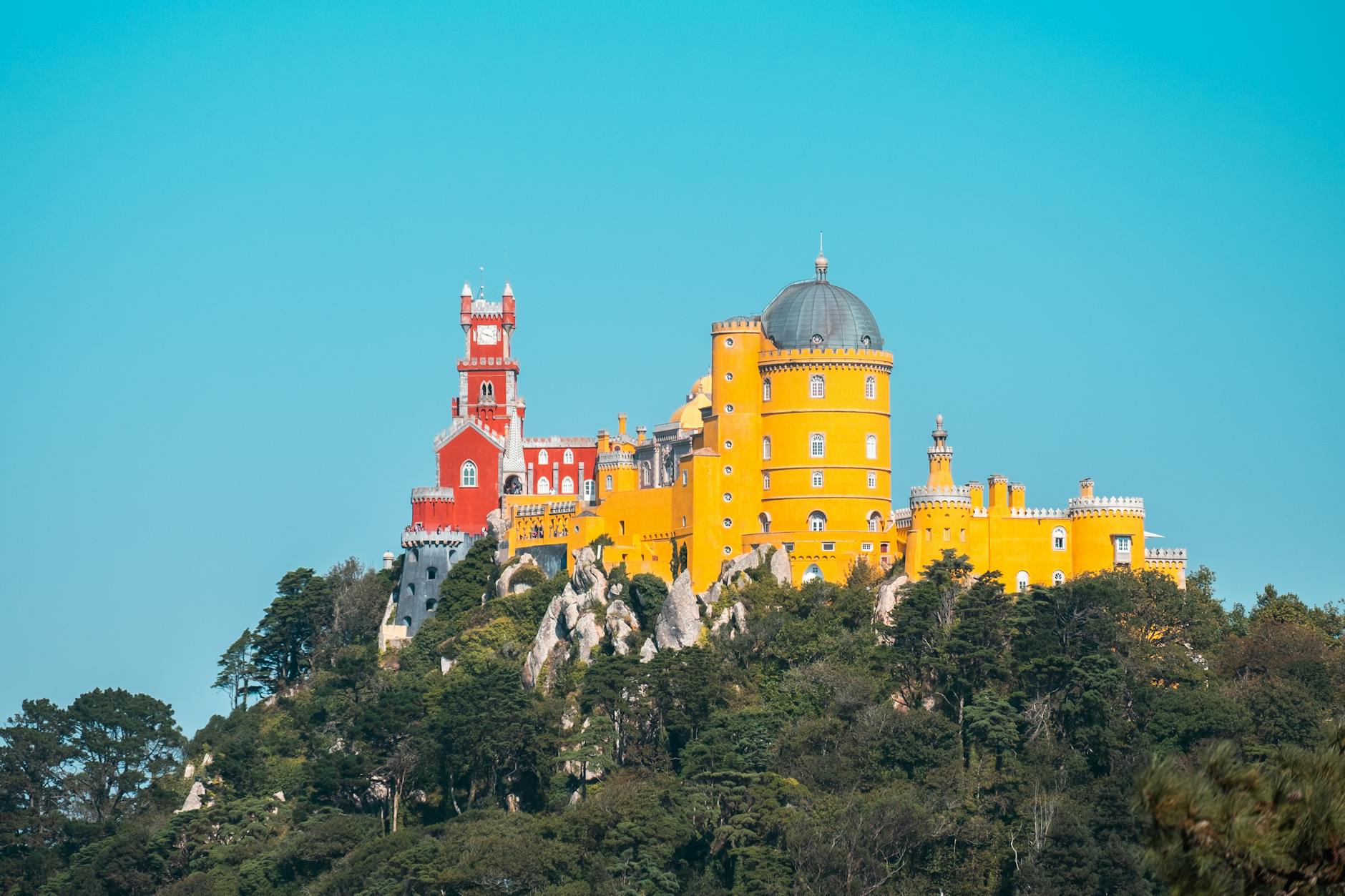 Pena Palace Sintra colorful red and yellow facade against blue sky and forested hills