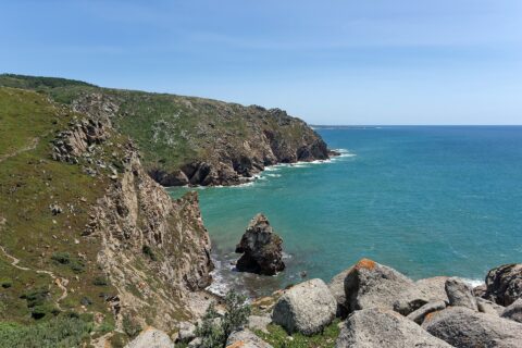 Cliffs at Cabo da Roca falling into a turquoise Atlantic bay, with a sea stack below and a footpath along the headland