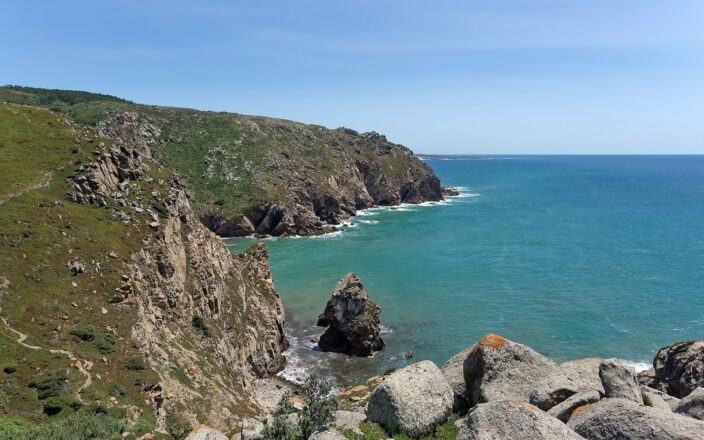 Cliffs at Cabo da Roca falling into a turquoise Atlantic bay, with a sea stack below and a footpath along the headland