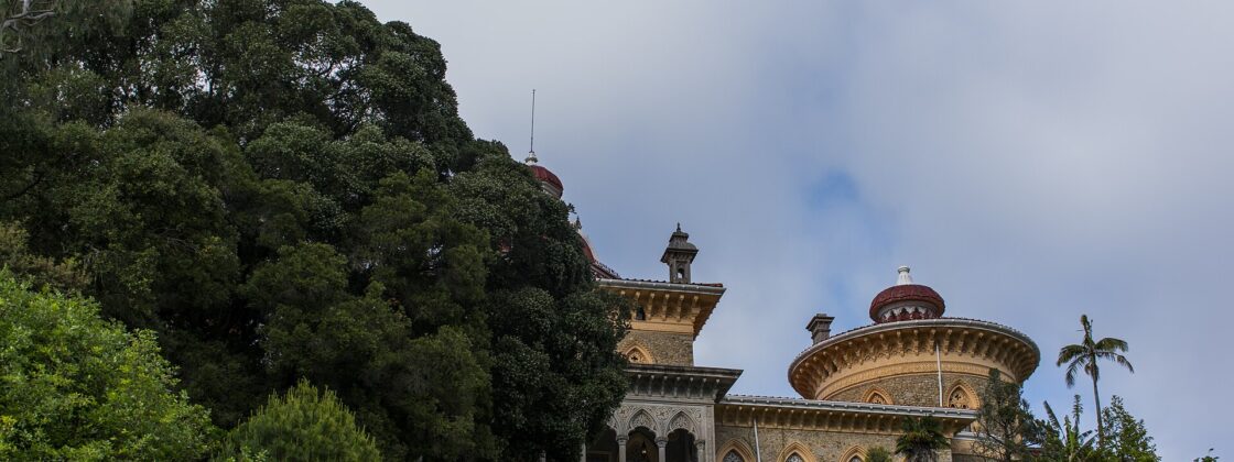 Monserrate Palace in Sintra seen across the Great Lawn, its yellow and red domes rising beside an enormous spreading tree