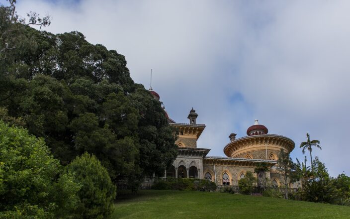 Monserrate Palace in Sintra seen across the Great Lawn, its yellow and red domes rising beside an enormous spreading tree