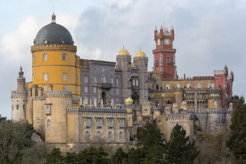 Pena Palace in Sintra, its yellow rotunda, lilac tiled wing and red clock tower rising above the treeline