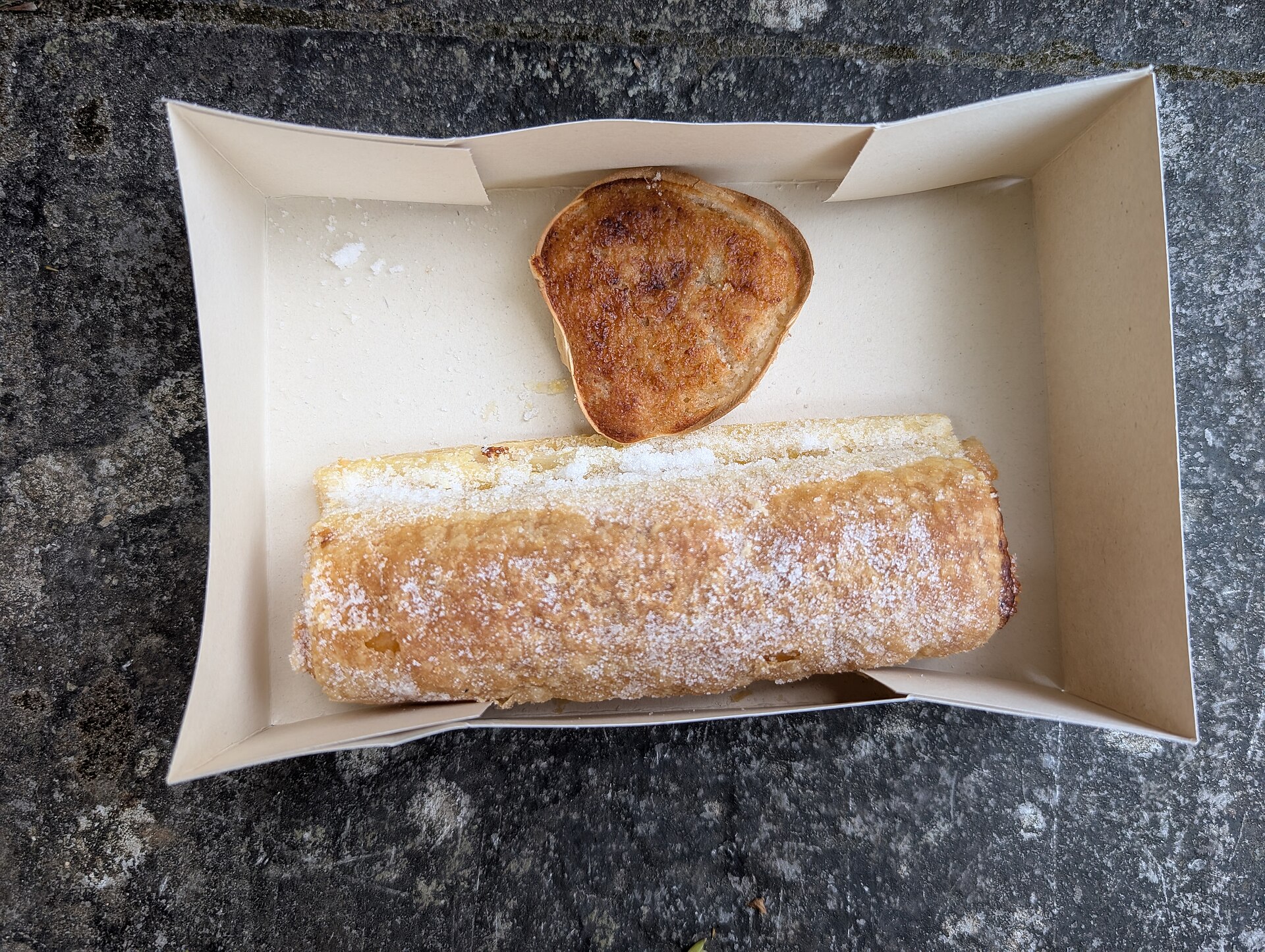 A travesseiro and a queijada de Sintra in a paper box, the travesseiro dusted with sugar
