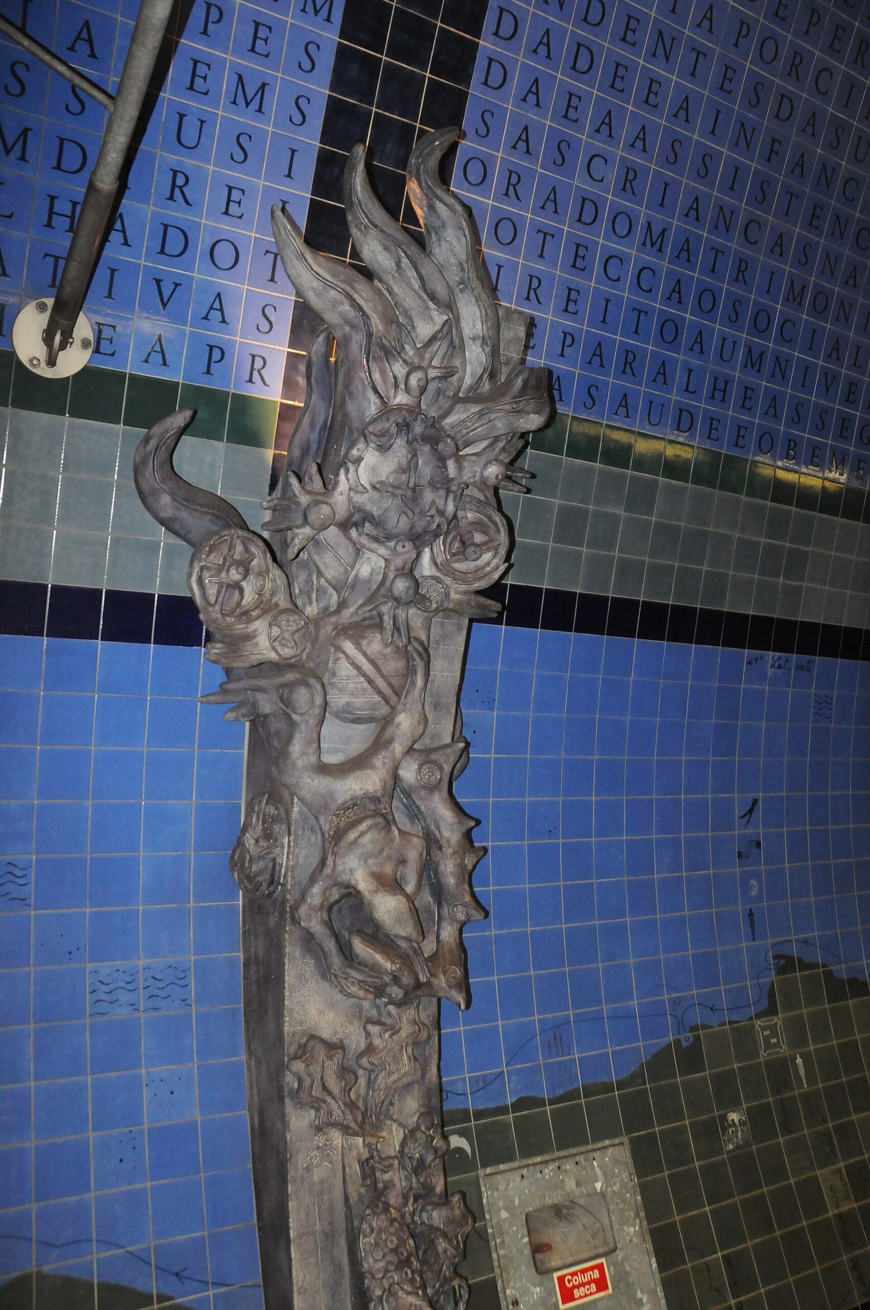 Blue azulejo panels with lettering and landscape motifs surround a sculpted column at Parque metro station in Lisbon.