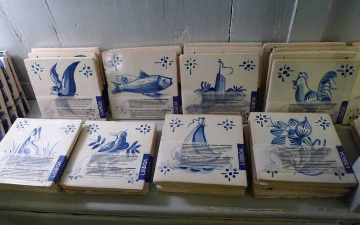 Blue-and-white souvenir tiles in a Lisbon shop depict birds, fish and flowers, with labels identifying hand-painted replicas.