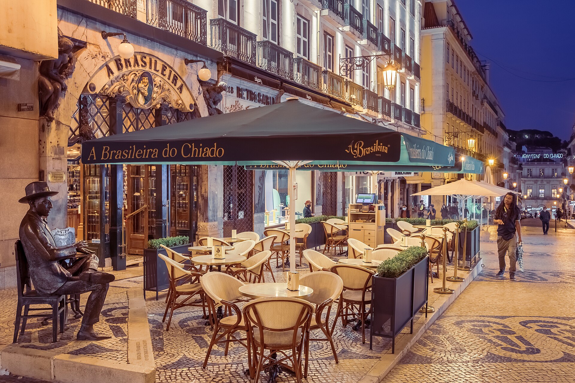 A Brasileira café in Lisbon’s Chiado district, with terrace tables, green awnings and the seated Fernando Pessoa statue at dusk.