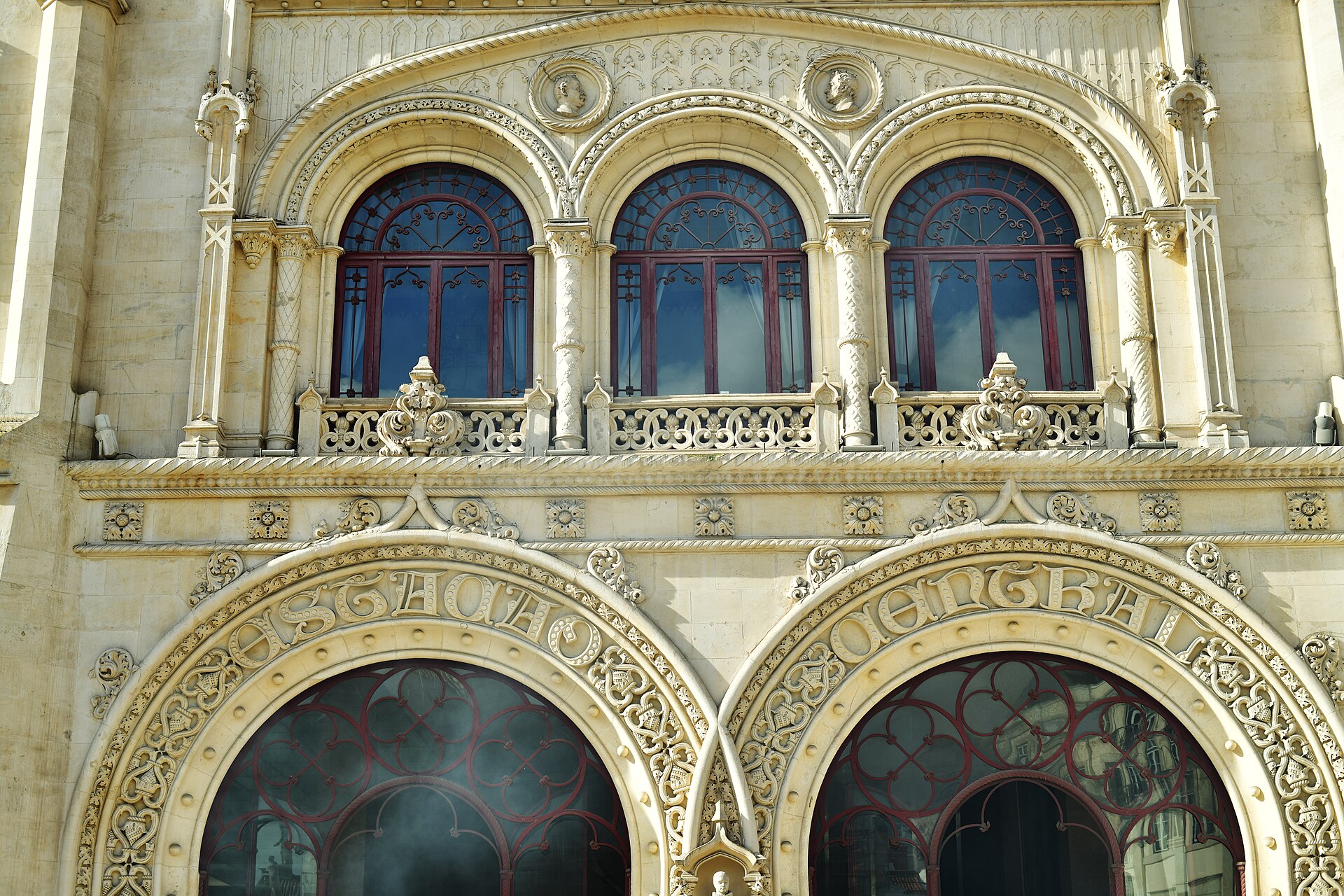 Carved stone horseshoe arches and red framed windows on Rossio railway station in Lisbon, with ornate lettering above the entrances.