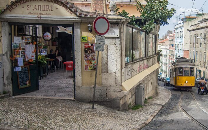 A chalkboard menu stands at Santo André restaurant in Lisbon, beside a yellow tram on the cobbled Calçada de Santo André.