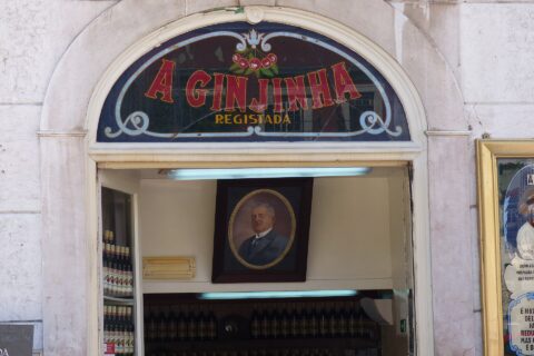 The cherry-decorated sign above A Ginjinha in Lisbon frames an open doorway with bottles and a portrait inside.
