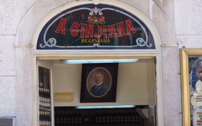 The cherry-decorated sign above A Ginjinha in Lisbon frames an open doorway with bottles and a portrait inside.