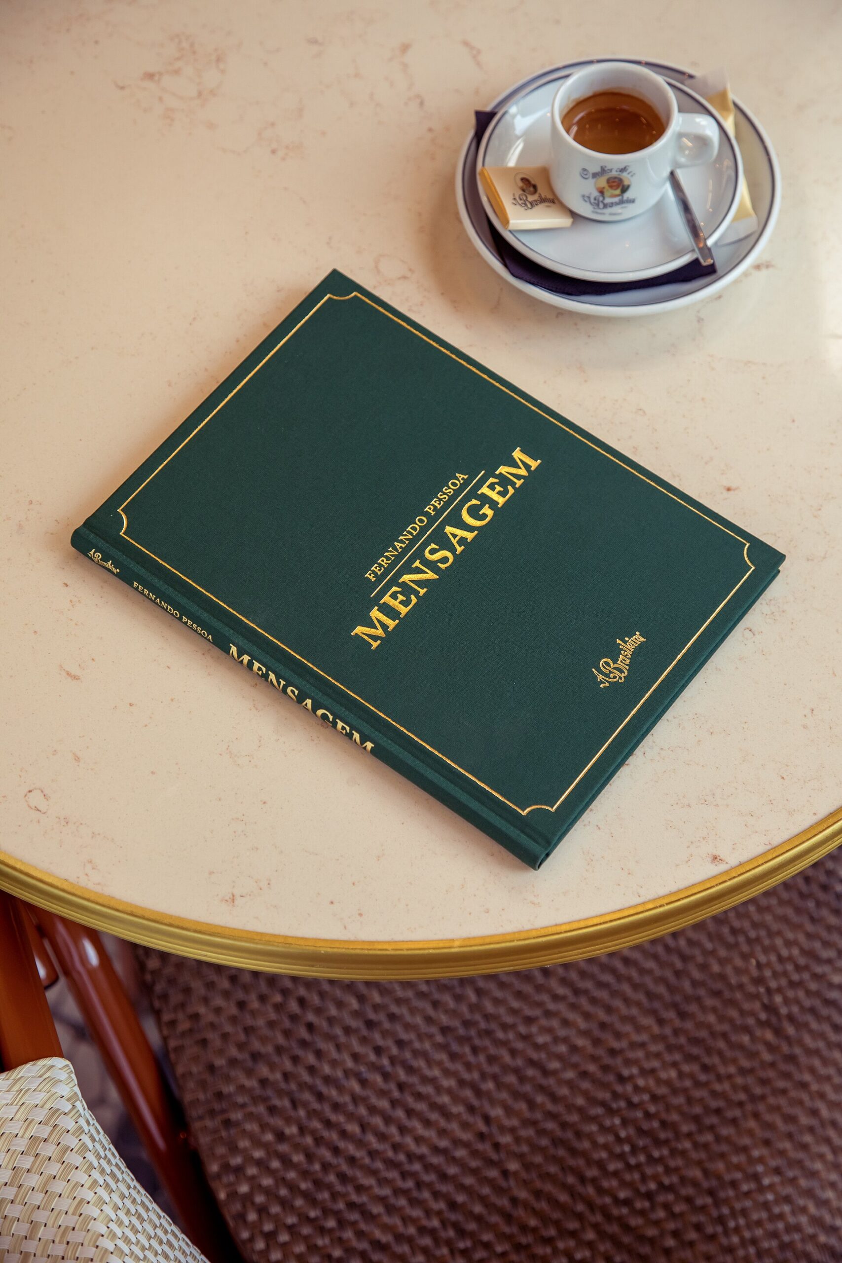 An espresso and Fernando Pessoa’s Mensagem sit on a pale marble table at A Brasileira café in Lisbon.