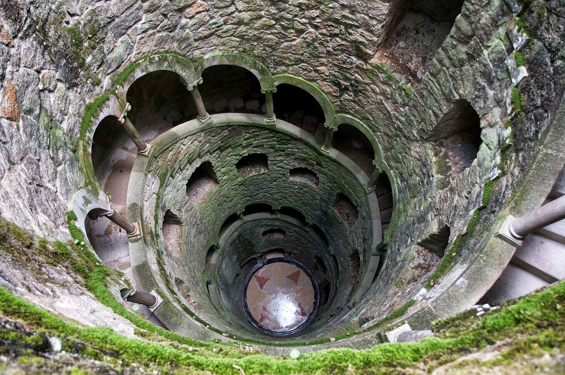 The Initiation Well at Quinta da Regaleira spirals downward through mossy stone arches toward a patterned circular floor.