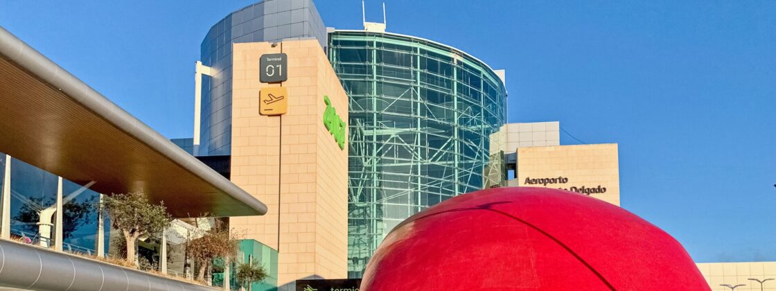 Lisbon Airport Terminal 1 rises behind the red dome of Aeroporto metro station as pedestrians cross the forecourt.