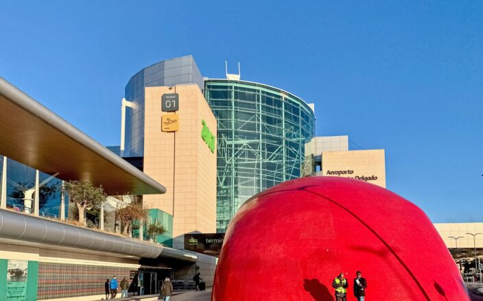 Lisbon Airport Terminal 1 rises behind the red dome of Aeroporto metro station as pedestrians cross the forecourt.