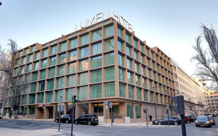 Lumen Hotel in Lisbon occupies a street corner, with tall windows and its name displayed above the roof.