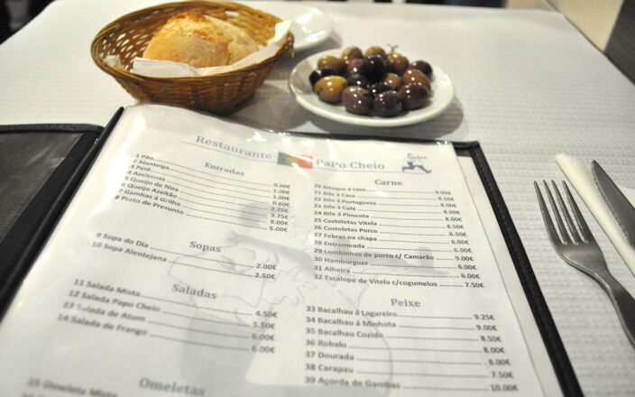 An open menu at PaPo Cheio in Lisbon lists Portuguese dishes and euro prices beside bread, olives and cutlery.