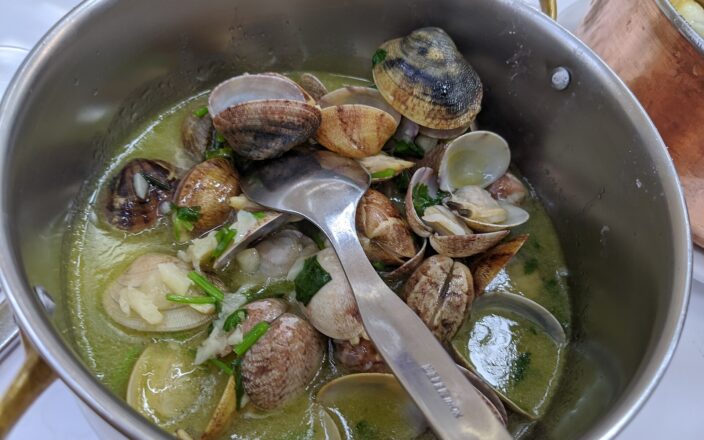 Opened clams with garlic and green herbs sit in a metal pan at Cervejaria Ramiro in Lisbon.