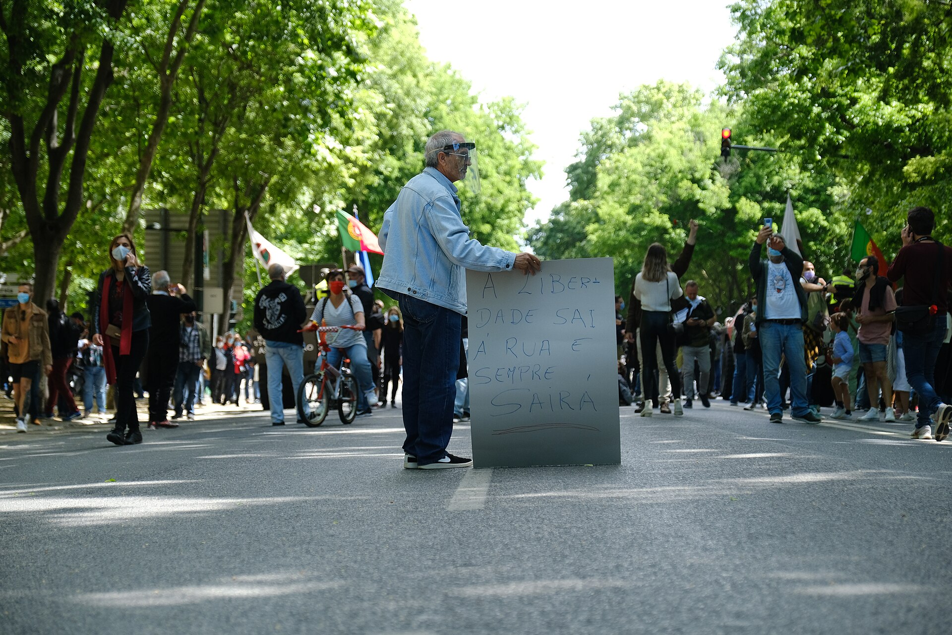 Participants with Portuguese flags and a handwritten liberty placard gather on Lisbon's tree-lined Avenida da Liberdade during the 25 April march.