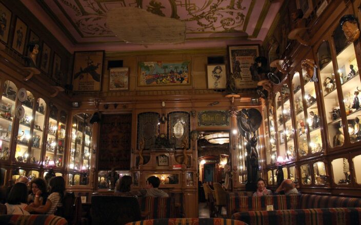 Patrons sit among striped armchairs and illuminated display cabinets beneath the ornate ceiling of Pavilhão Chinês bar in Lisbon.