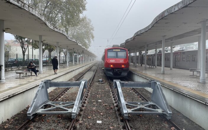 Red CP suburban train at Sintra station between covered platforms, with passengers waiting beside the tracks on a misty morning.