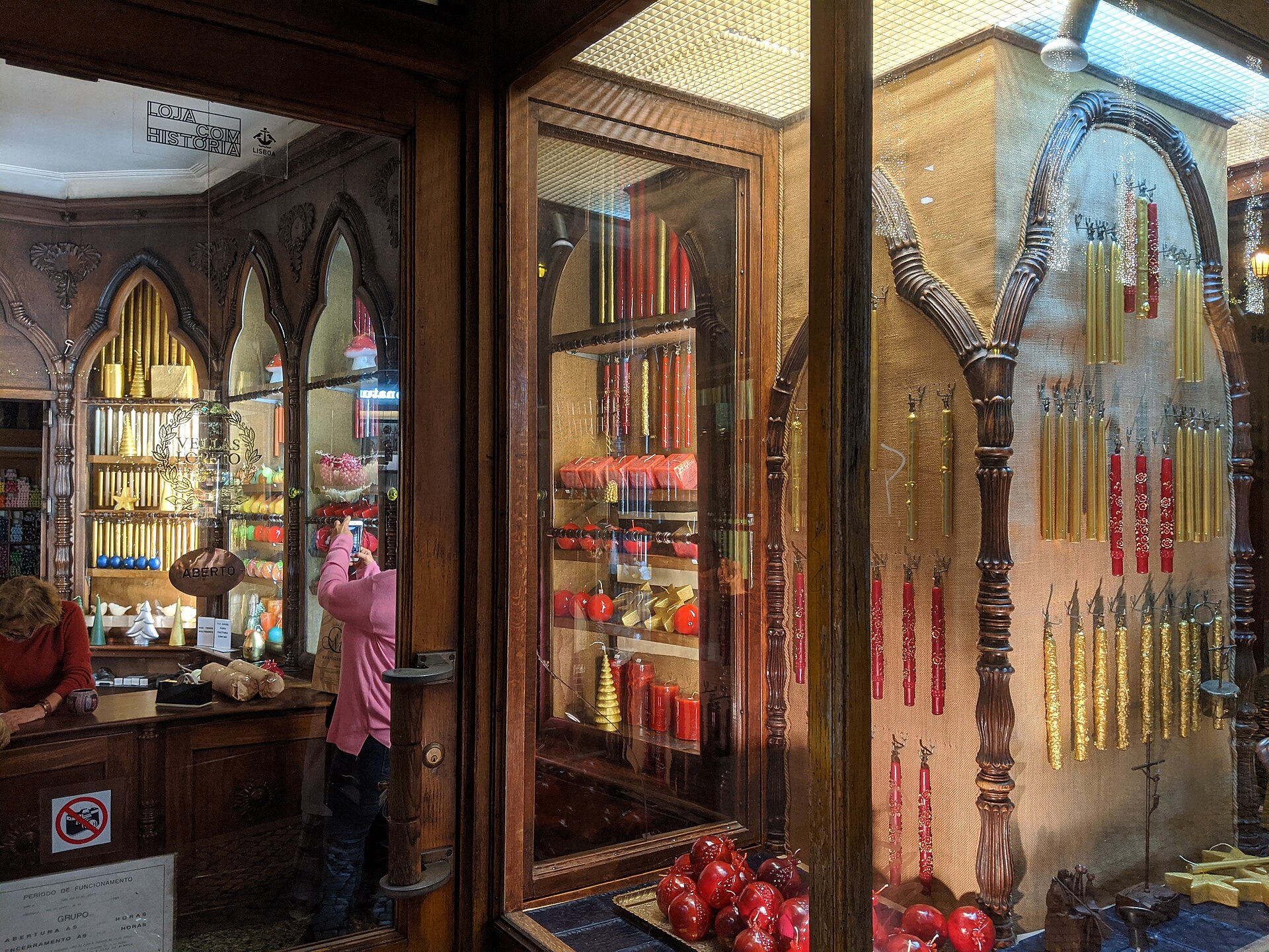 Red and gold candles fill ornate wooden displays at Lisbon’s Caza das Vellas Loreto, with shoppers visible through the doorway.