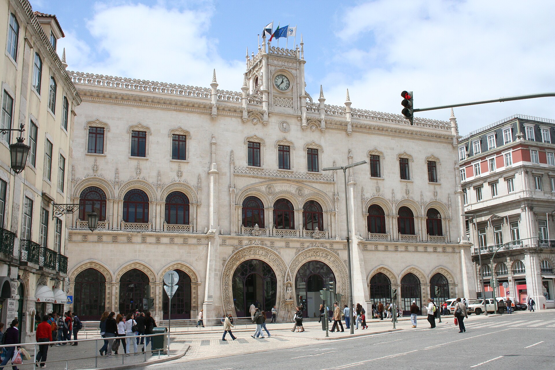 Rossio railway station in Lisbon with its pale neo-Manueline facade, central clock, horseshoe entrances and pedestrians crossing outside.