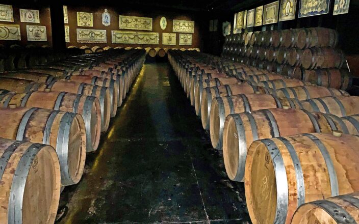 Rows of wine barrels fill Bacalhôa’s cellar in Azeitão, with decorative Portuguese tile panels lining the walls above them.