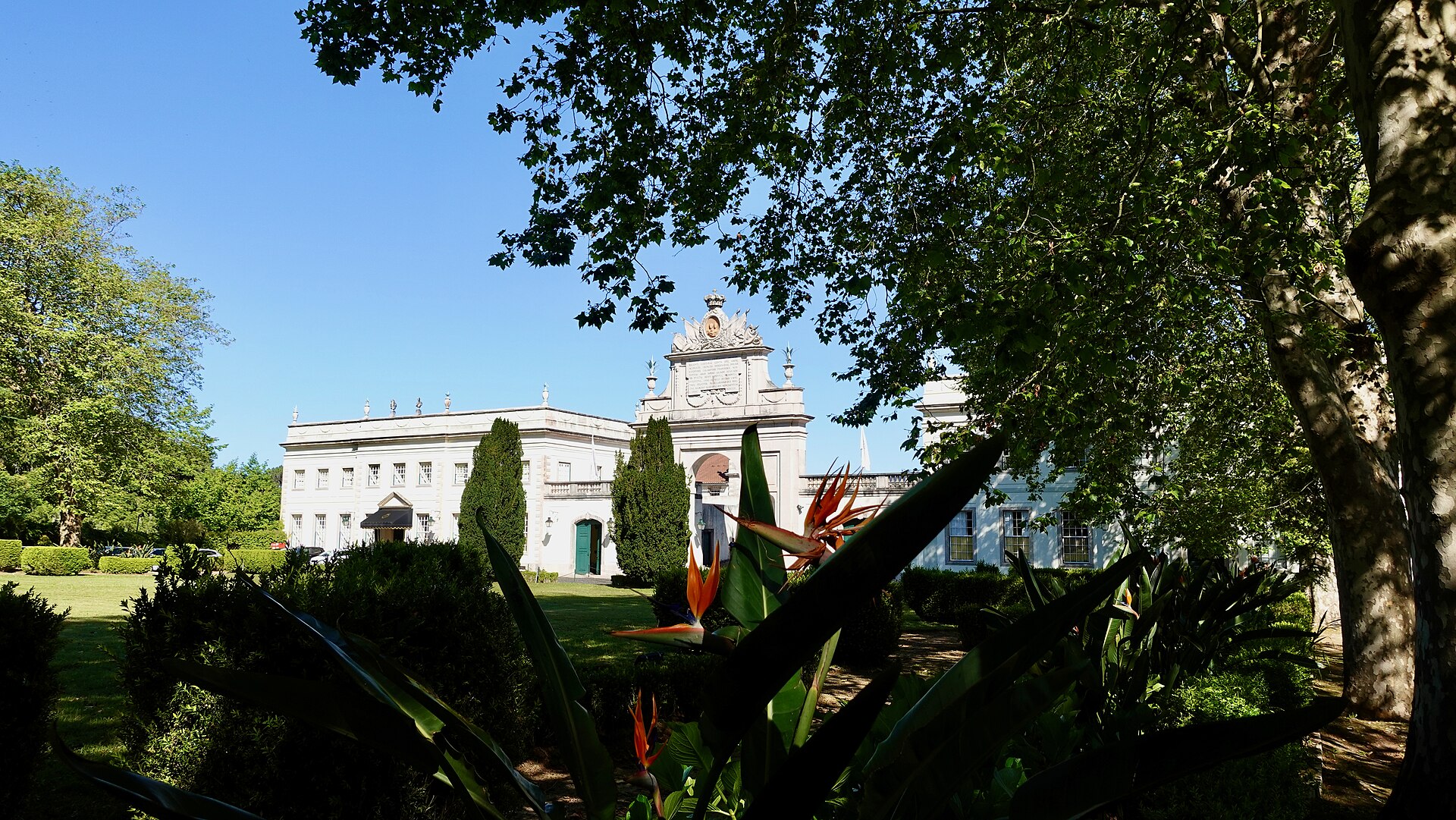 The Seteais palace hotel in Sintra stands beyond a green lawn, with an ornate arch framed by trees.
