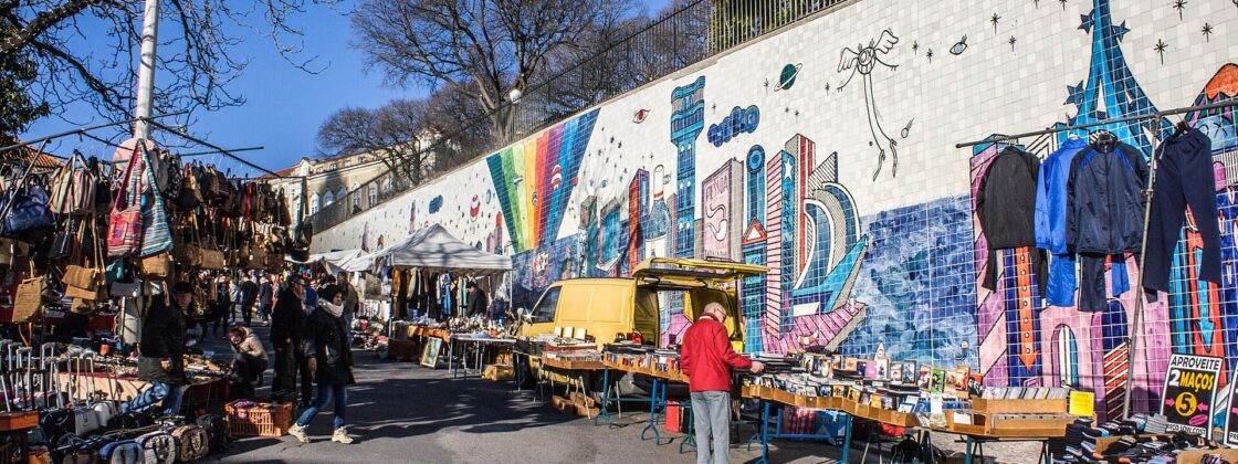 Shoppers browse records, bags and clothing beside the colorful tile mural at Feira da Ladra in Lisbon.