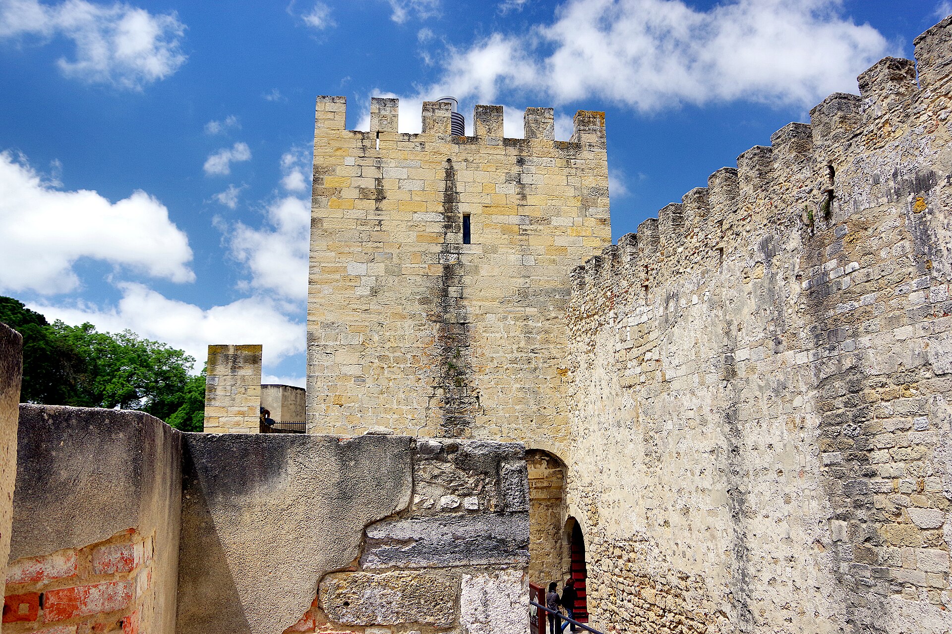 A square stone tower and crenellated walls rise above an arched passage at São Jorge Castle in Lisbon.