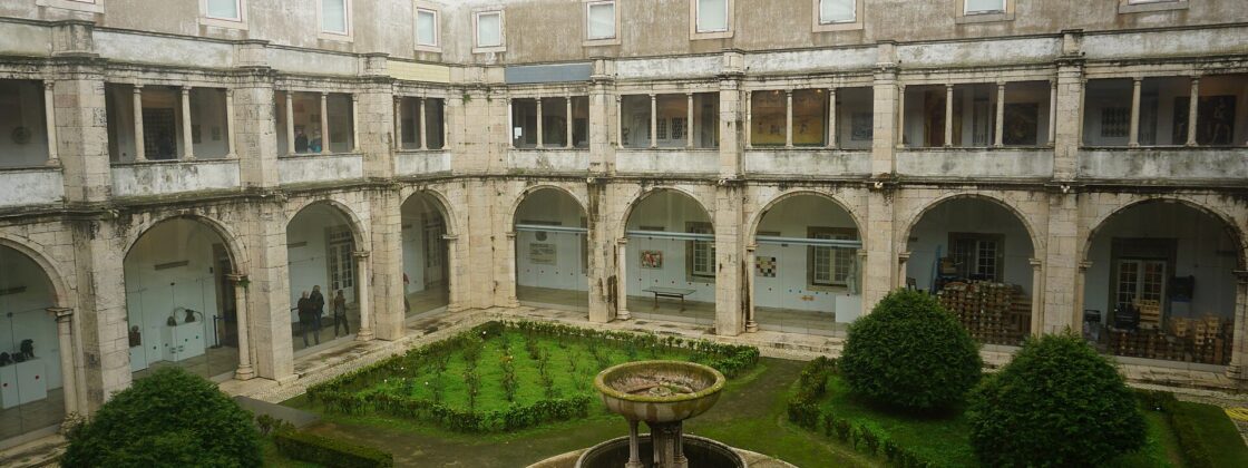 A stone fountain and clipped shrubs fill the National Tile Museum's cloister in Lisbon, surrounded by arcades and glazed galleries.