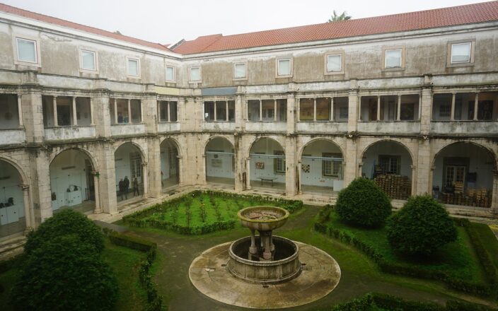 A stone fountain and clipped shrubs fill the National Tile Museum's cloister in Lisbon, surrounded by arcades and glazed galleries.