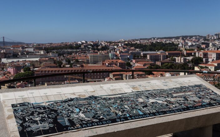 A tiled orientation panel at Miradouro da Senhora do Monte identifies Lisbon landmarks above a panorama of red rooftops.