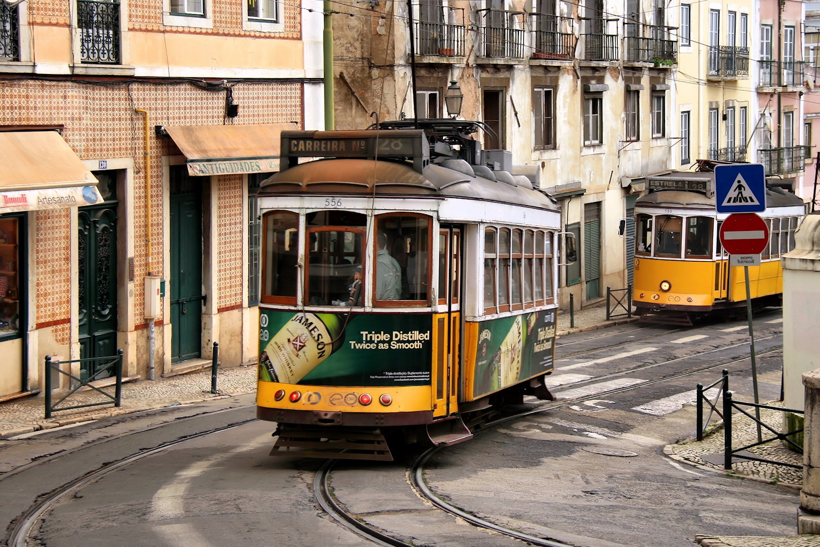 Two yellow Tram 28 cars follow curved rails between tiled buildings in Lisbon, with an Estrela destination board visible.