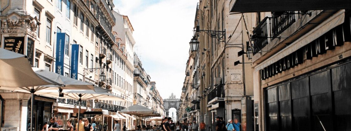 Visitors and cafe tables line Lisbon’s Rua Augusta, with patterned paving leading toward the triumphal arch.